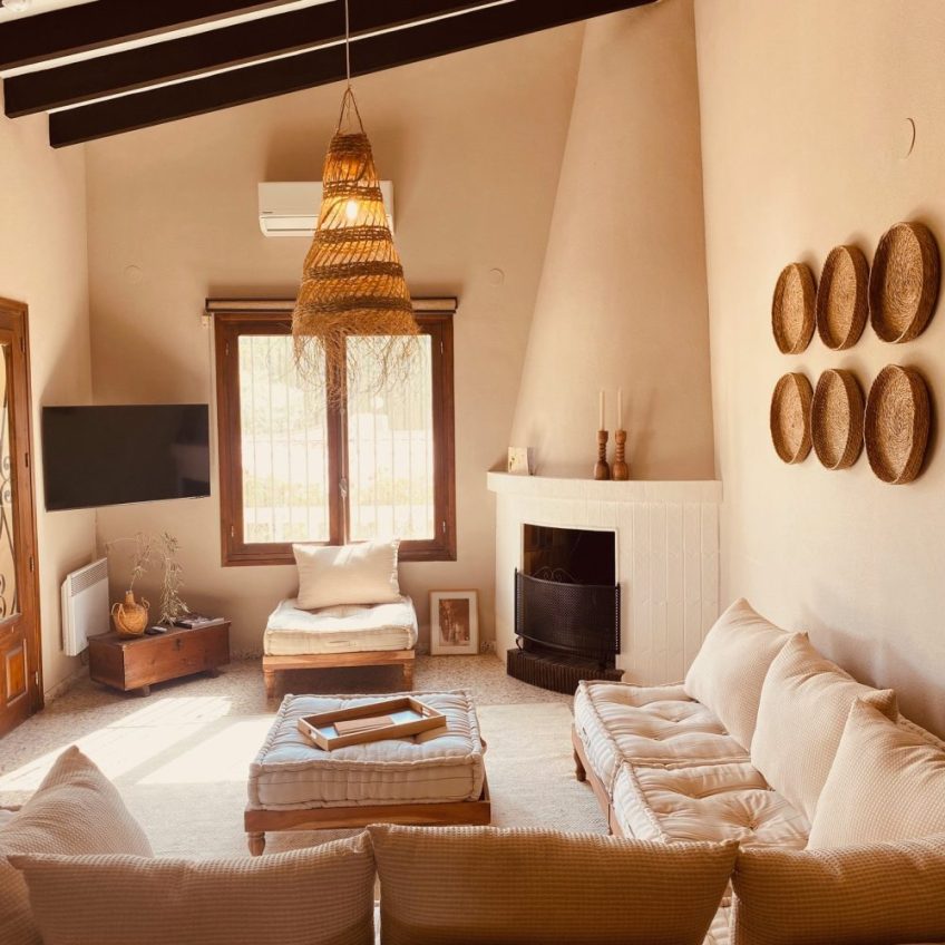 Casa Orange Moraira: metamorfose van mediterraanse villa, verbouwd met behoud van originele terrazzo vloertegels uit 1974, open haard en hoge plafonds. Ingericht met lokaal vervaardigde materialen uit de regio. Wat een sfeervolle woonkamer is het geworden!